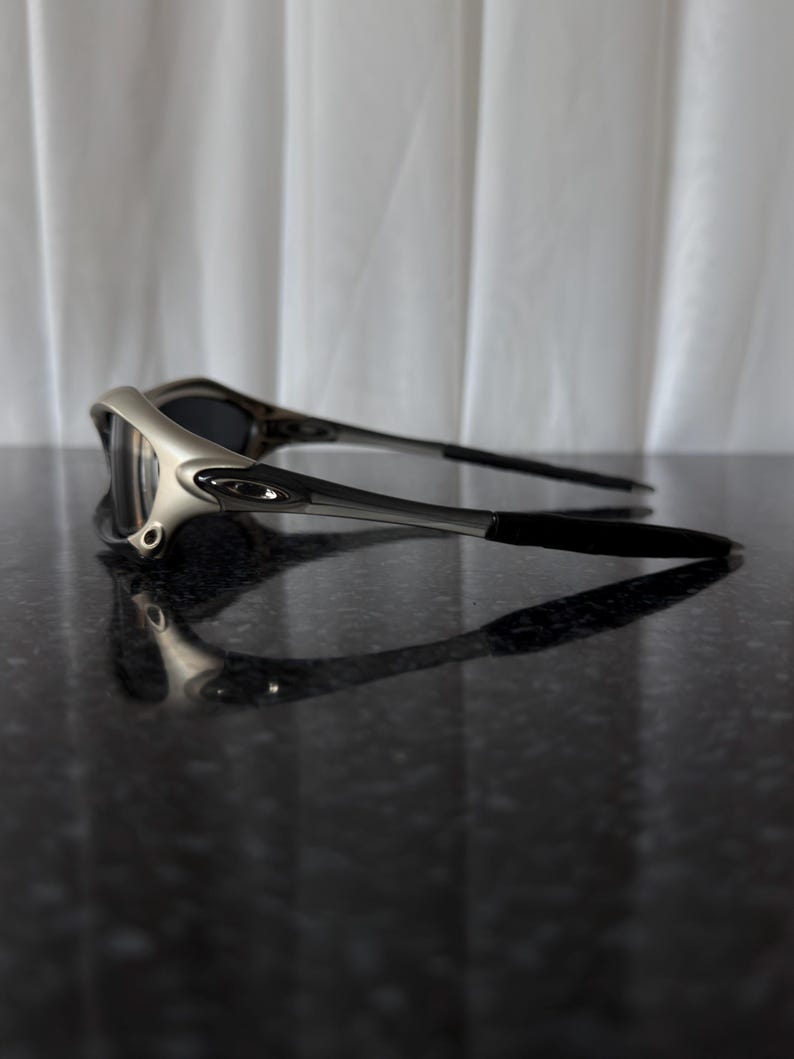 May include: Silver and black sunglasses with dark lenses. The sunglasses have a sleek, modern design with a silver frame and black arms. The lenses are dark, providing shade and protection from the sun.