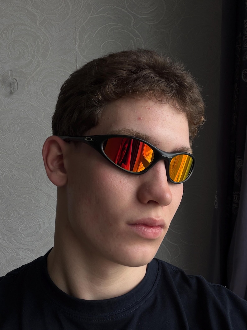 May include: Black sunglasses with a curved frame and reflective orange and red lenses. The sunglasses are worn by a person wearing a black shirt.