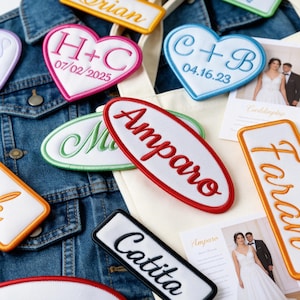 May include: A collection of embroidered patches in different shapes, including hearts and ovals, with names and dates. The patches are white with colourful borders and lettering. Some are displayed on a denim jacket and a tote bag.