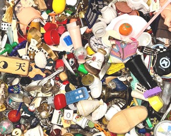May include: A jumble of miniature items, including figurines, buttons, and dice. The collection features a variety of colours and shapes, with objects such as a lighthouse, a chess piece, and a small blue police box. The items are scattered in a container.