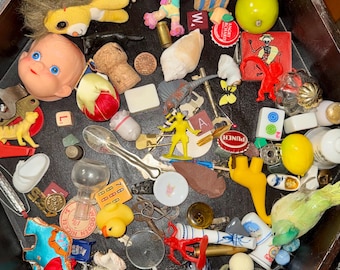 May include: A collection of miscellaneous small objects inside a dark wooden box, including a doll head, a yellow plush lion, a rubber duck, plastic toy figures, metal keys, bottle caps, game tiles, a seashell, and various miniature trinkets.