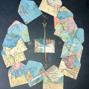 May include: A compass with a gold needle surrounded by eight small envelopes. Each envelope is decorated with a map of a different location. The envelopes are arranged in a circle around the compass.