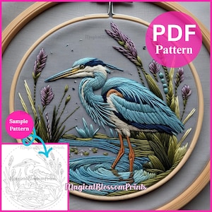 Puede incluir: Arte de aro bordado con una garza azul en una escena de pantano. La garza tiene plumas azules y blancas, con patas naranjas y un largo pico amarillo. El fondo es gris, con plantas verdes y moradas. El texto "PDF Pattern" está en un círculo rosa.