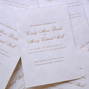 Op de afbeelding: Een stapel ivoorkleurige trouwuitnodigingen met gouden belettering. De uitnodigingen kondigen de bruiloft van Cecily Alicia Banks en Henry Edward Sholl aan, gepland voor 18 oktober 2025.