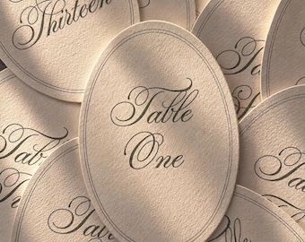 Könnte beinhalten: Eine Sammlung ovaler Tischkarten. Jede Karte ist hellbeige mit einem dunkelgrauen Rand und eleganter Schrift. Die Karten sind von eins bis dreizehn nummeriert und eignen sich perfekt für Hochzeiten oder Veranstaltungen.