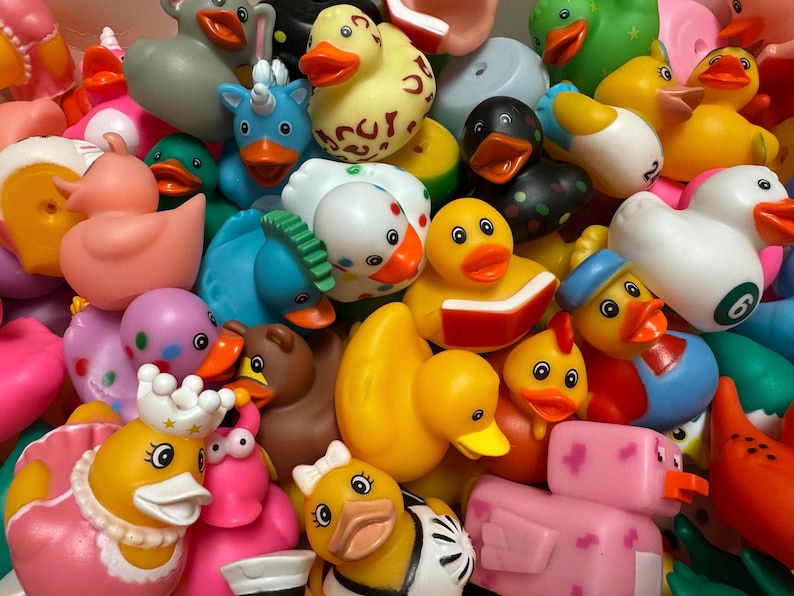 May include: A colorful assortment of rubber duck toys in various designs and colors. The collection includes ducks with hats, crowns, and other accessories. Some ducks are reading books, and others have unique patterns.