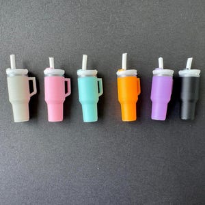 May include: Six miniature tumblers in various colors: beige, pink, teal, orange, purple, and black. Each tumbler has a white lid and a white straw. The tumblers have a handle on the side.