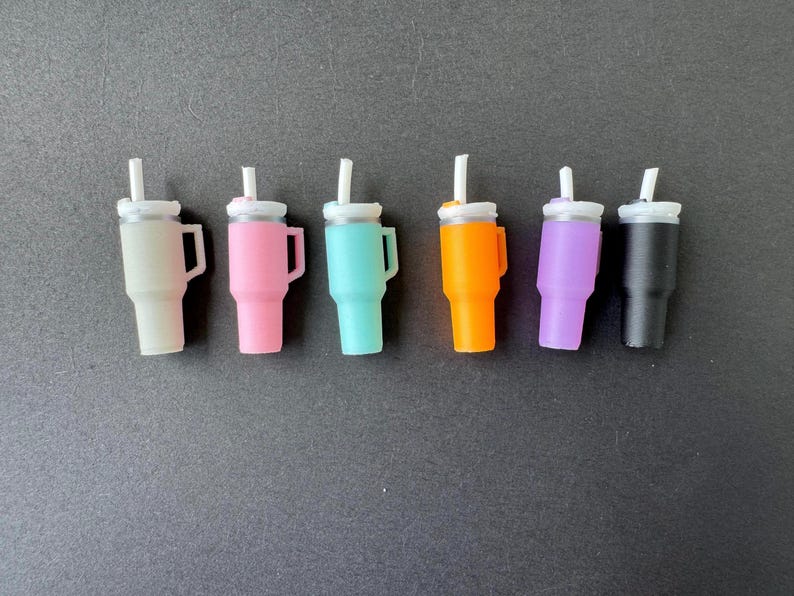 May include: Six miniature tumblers in various colors: beige, pink, teal, orange, purple, and black. Each tumbler has a white lid and a white straw. The tumblers have a handle on the side.