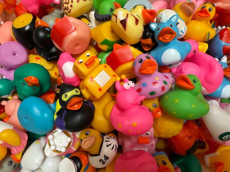 May include: A vibrant assortment of rubber duck toys in various colors and designs. The collection includes ducks in shades of yellow, pink, green, blue, and black, some with unique patterns and accessories. A playful and colorful collection.