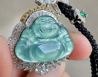 May include: A pendant featuring a translucent light green carved jade figure of a laughing Buddha, framed by white diamonds and yellow sapphires in a silver-toned setting, attached to a black braided cord with a small green stone accent.