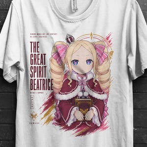 May include: A white t-shirt featuring a graphic of a blonde anime character with twin drills, wearing a maroon dress with white trim and a crown. The text reads THE GREAT SPIRIT BEATRICE, with additional Japanese characters and abstract pink brush strokes.