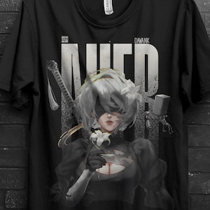 Könnte beinhalten: Schwarzes T-Shirt mit einer detaillierten Illustration eines Charakters mit weißen Haaren und Augenbinde, der eine Blume und ein Schwert hält. Das Wort "NIER" ist in großen, weißen Buchstaben gedruckt. Das T-Shirt hängt an einem schwarzen Kleiderbügel.