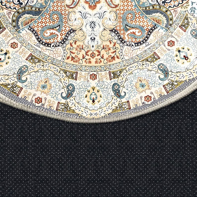 Puede incluir: Primer plano de una alfombra redonda con un intrincado dise&ntilde;o floral y paisley. La alfombra presenta un fondo crema con patrones en tonos azules, marrones y beige. El borde de la alfombra es visible, con un reverso azul oscuro punteado.