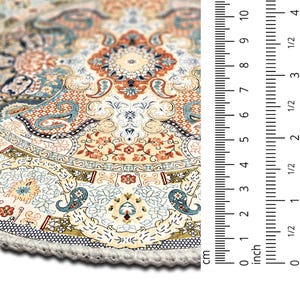 Puede incluir: Primer plano de una alfombra redonda con un patr&oacute;n intrincado y flecos color crema. La alfombra presenta un dise&ntilde;o floral detallado en tonos beige, naranja y azul. La regla muestra una medida de 10 cm.