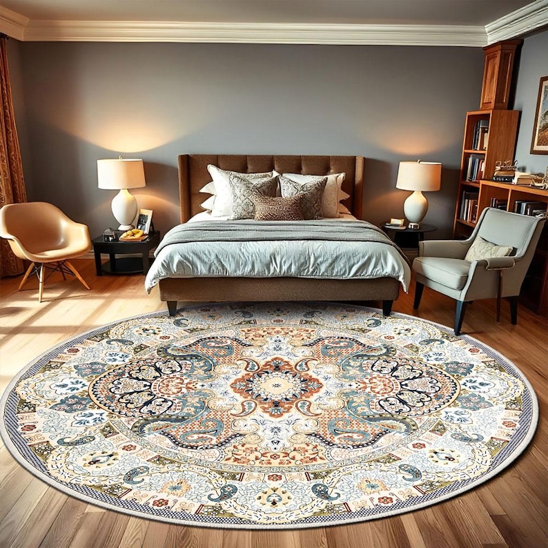 Puede incluir: Una alfombra redonda grande con un dise&ntilde;o intrincado y ornamentado. La alfombra presenta un fondo color crema con un patr&oacute;n detallado en tonos de azul, naranja y marr&oacute;n. La alfombra est&aacute; colocada en un dormitorio con una cama, una silla y un suelo de madera.