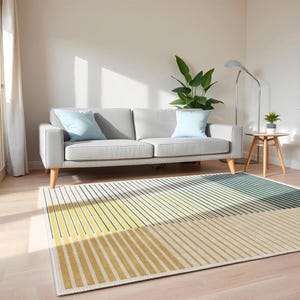 May include: A contemporary living room with a light grey sofa and two pale blue cushions. A rug with yellow, blue, and cream stripes lies on the floor. A small wooden side table and a floor lamp are also present.