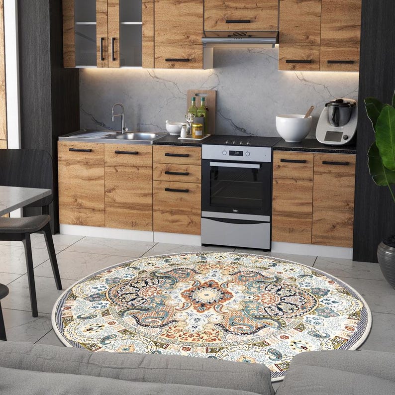 Puede incluir: Una cocina con armarios de madera, un fregadero de acero inoxidable y un horno negro. En el suelo hay una alfombra redonda con un estampado floral en tonos azules, naranjas y crema. Un sof&aacute; gris est&aacute; en primer plano. El di&aacute;metro de la alfombra es de unos 200 cm.