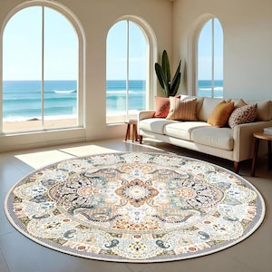May include: A round area rug with an intricate, ornate design. The rug features a cream-colored background with a detailed pattern in shades of blue, orange, and brown. The rug is placed in a living room with a sofa and large windows overlooking the ocean.