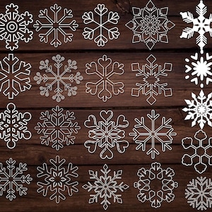 May include: A collection of twenty-one white snowflake designs on a dark brown wooden background. The snowflakes vary in shape and size, with intricate details and symmetrical patterns. Ideal for winter-themed crafts and decorations.