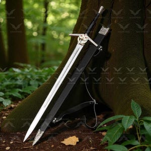 Pode incluir: Uma espada prateada e preta com punho e guarda decorativos, numa bainha preta. A espada está encostada a um tronco de árvore numa floresta. A bainha tem uma extremidade prateada decorativa.