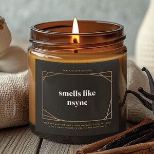 May include: A brown glass candle jar with a black label that reads "smells like nsync". The candle is lit and the label also says "Coconut Apricot Wax | 100% Natural & Eco Friendly | 4 oz | Hand Poured in USA | Made with Love."