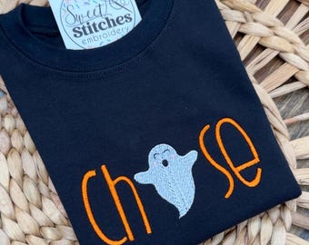 May include: Black t-shirt with orange embroidered text spelling "CHOOSE" and a light blue ghost graphic. A small sticker with the text "Sweet Stitches Embroidery" is visible.