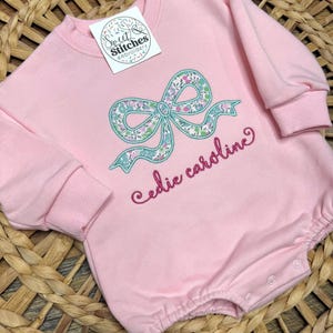 May include: Pink baby onesie with a floral bow and the name "Cedie Caroline" embroidered on the front.