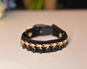 May include: A black and gold dog collar with a row of black and gold teardrop-shaped charms and clear rhinestones.