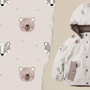 Könnte beinhalten: Eine hellfarbene Kinderjacke mit Kapuze und einem sich wiederholenden Muster aus Bären- und Dachsgesichtern. Die Jacke hat ein braunes Innenfutter und Taschen. Der Hintergrund zeigt das gleiche Muster auf einer hellbraunen Oberfläche.