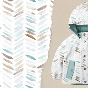 Könnte beinhalten: Eine weiße Kapuzenjacke mit einem Aquarell-Chevron-Muster in Blau-, Braun- und Beigetönen. Die Jacke hat ein türkisgrünes Futter und Akzente, mit zwei Vordertaschen und Druckknöpfen. Das Muster befindet sich auch im Hintergrund.