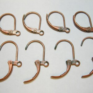 May include: Eight copper-colored earring hooks are displayed against a white background. The hooks are in two rows, with the top row closed and the bottom row open. Each hook has a curved wire and a hinged lever.