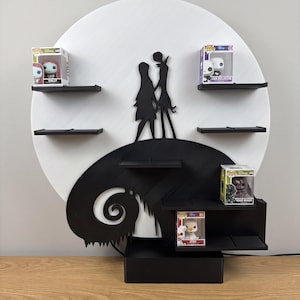 Peut inclure: Étagère décorative noire et blanche représentant une silhouette de Jack et Sally de L'Étrange Noël de Monsieur Jack. L'étagère a plusieurs niveaux et un design circulaire avec un fond de lune. Plusieurs figurines de personnages sont exposées.