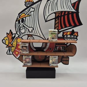 Op de afbeelding: Een houten plank in de vorm van een schip, met meerdere niveaus voor het tentoonstellen van verzamelobjecten. Het scheepsontwerp omvat zwart-witte zeilen, een schedel en gekruiste botten en rood-zwarte accenten. Verschillende Funko Pop-figuren worden tentoongesteld.