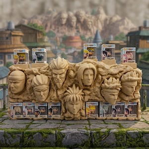 Peut inclure: Présentation de figurines Funko Pop Naruto, sur fond de monument en pierre sculptée avec des visages de personnages. L'exposition comprend plusieurs figurines en boîte et une base en pierre avec des visages sculptés, le tout sur une surface en pierre.