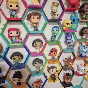 Può includere: Un'unità a scaffale esagonale con ripiani colorati presenta una varietà di figurine della cultura pop. Le figurine includono personaggi Disney, Pixar e altri franchise popolari. L'unità a scaffale è un ottimo modo per esporre e organizzare le tue collezioni preferite.