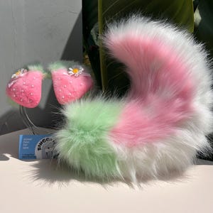 May include: A colourful cosplay set with a fluffy tail and strawberry-shaped ears. The tail is a blend of green, pink, and white faux fur. The ears are pink with white dots and a daisy detail. Ideal for themed events or costume parties.