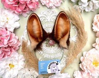 May include: Faux fur animal ears on a headband, with brown and tan fur, surrounded by pink and white flowers. A small card with a cartoon walrus and the text "Animal faux fur ears" is visible.