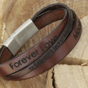 K&ouml;nnte beinhalten: Braunes Lederarmband mit einem silbernen Verschluss. Das Armband ist mit den Worten "Forever Love" und "Still Like a Melody" graviert.