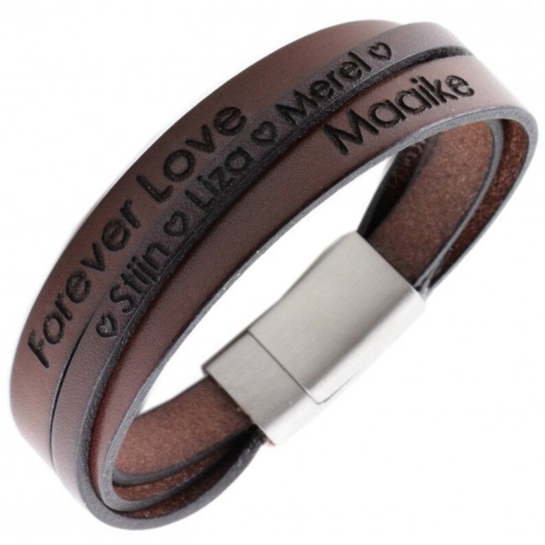 K&ouml;nnte beinhalten: Braunes Lederarmband mit einem Edelstahlverschluss. Das Armband hat zwei B&auml;nder mit dem Text "Forever Love" und "Still Liza & Merel" auf einem Band und "Maaike" auf dem anderen Band.