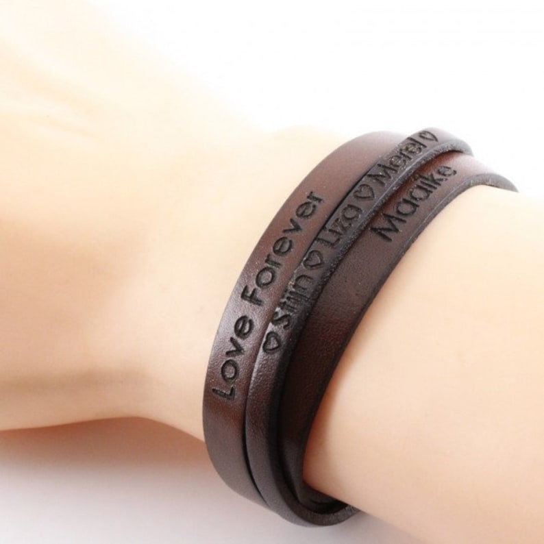 K&ouml;nnte beinhalten: Braunes Lederarmband mit den Worten "Love Forever", "Justin Leo" mit einem Herzsymbol und "Malika" eingraviert.