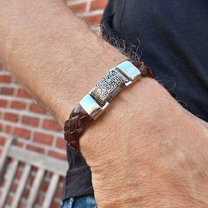 Puede incluir: Un brazalete de cuero marrón con un cierre plateado con un diseño de huella digital.