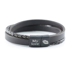 Puede incluir: Una pulsera de cuero gris oscuro con un dise&ntilde;o de doble hebra, que incluye una banda lisa y una banda trenzada. La pulsera cuenta con un cierre magn&eacute;tico de metal negro grabado con el texto My love y un gr&aacute;fico de labios.