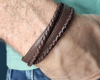 May include: A brown leather bracelet with a braided design. The bracelet is made of three strands of leather that are woven together.