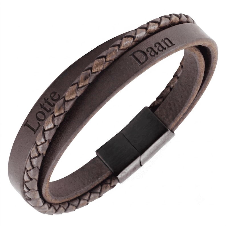 Puede incluir: Una pulsera de cuero marr&oacute;n que presenta una hebra trenzada y una banda plana lisa grabada con los nombres Lotte y Daan. La pulsera se asegura con un cierre magn&eacute;tico rectangular de metal negro, creando una apariencia superpuesta.