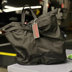 May include: A black nylon travel bag with a red and black zipper and a black tag that says "STEVENS" in red letters.