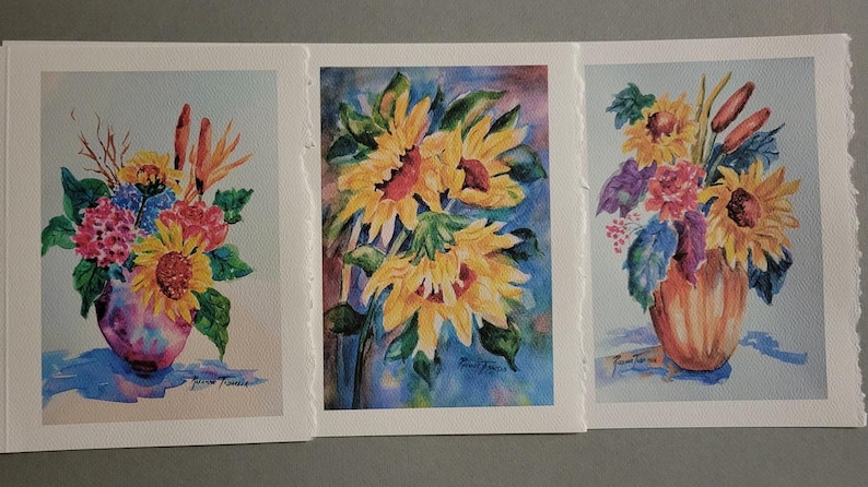 May include: Three watercolor paintings of floral arrangements in vases. The first painting features a pink vase with a bouquet of yellow, orange, red, and blue flowers. The second painting features a blue vase with a bouquet of yellow sunflowers. The third painting features an orange vase with a bouquet of yellow sunflowers, red and purple flowers, and green leaves.