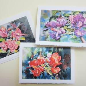 May include: Three watercolor paintings of bougainvillea flowers. The first painting features pink flowers with dark green leaves against a dark background. The second painting features purple flowers with green leaves against a light blue background. The third painting features red flowers with green leaves against a dark blue background.