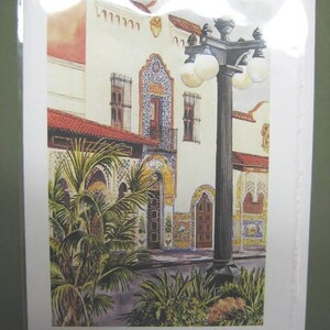 Op de afbeelding: Een aquarel van een wit gebouw met een betegelde gevel en een lantaarnpaal ervoor. Het gebouw heeft een rood pannendak en een balkon met een smeedijzeren balustrade. De lantaarnpaal is zwart met een gouden top en heeft meerdere lampen. Op de voorgrond staan groene planten.