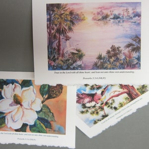 Peut inclure: Trois aquarelles avec des citations inspirantes. La premi&egrave;re peinture repr&eacute;sente une fleur de magnolia blanche avec des feuilles vertes sur un fond p&ecirc;che. La deuxi&egrave;me peinture montre un h&eacute;ron blanc debout dans un marais avec des palmiers et un coucher de soleil en arri&egrave;re-plan. La troisi&egrave;me peinture montre un oiseau rouge perch&eacute; sur une branche avec des feuilles vertes et un ciel bleu en arri&egrave;re-plan. Les trois peintures incluent la citation "Fais confiance &agrave; l'&Eacute;ternel de tout ton c&oelig;ur, et ne t'appuie pas sur ta propre intelligence. Proverbes 3:5-6 (NKJV)"