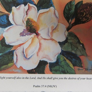 Peut inclure: Une peinture &agrave; l'aquarelle d'une fleur de magnolia blanche avec des feuilles vertes et un bourgeon brun. La peinture contient une citation de la Bible, Psaume 37:4 (NKJV) : "D&eacute;lecte-toi aussi en l'&Eacute;ternel, et il te donnera ce que ton c&oelig;ur d&eacute;sire."
